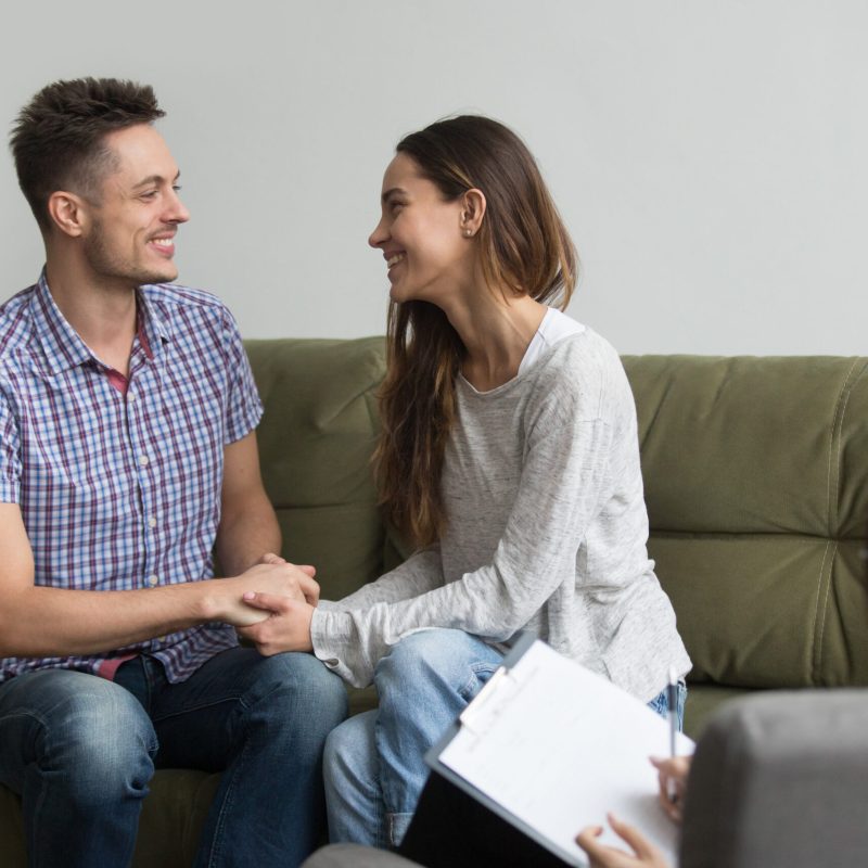 couple tharepy Happy young couple smiling reconciled after quarrel, holding hands and looking into eyes after positive therapy treatment session from psychologist. Concept of saved marriage, spouses making peace